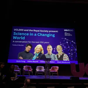 Stage with a large screen reading 'Science in a Changing World' and four panelists pictured, podium center, chairs on stage, audience in front.