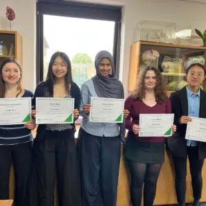 Five students stand side by side in a science classroom, each holding a certificate of achievement for the Cambridge Biology Challenge.