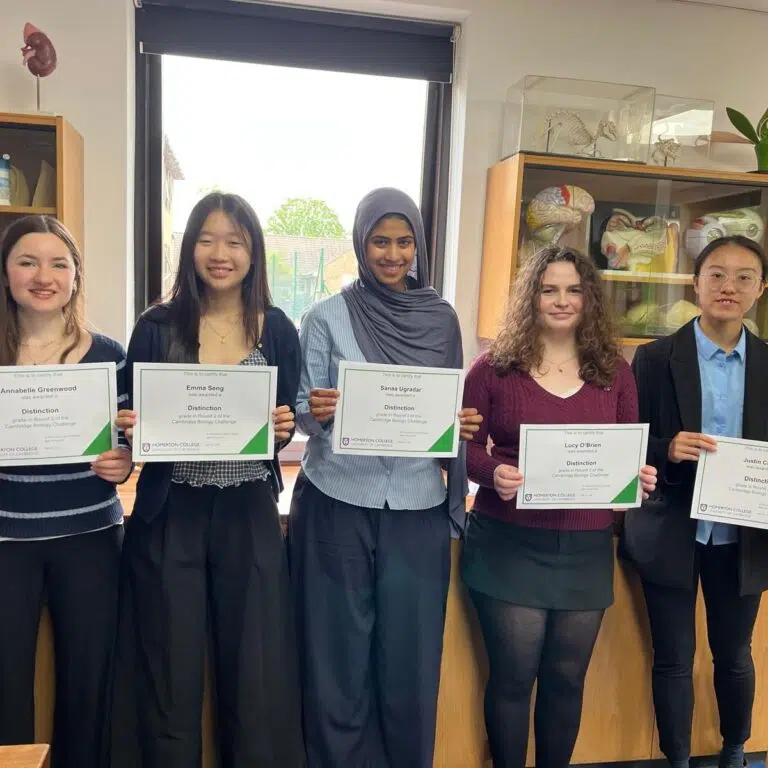 Five students stand side by side in a science classroom, each holding a certificate of achievement for the Cambridge Biology Challenge.
